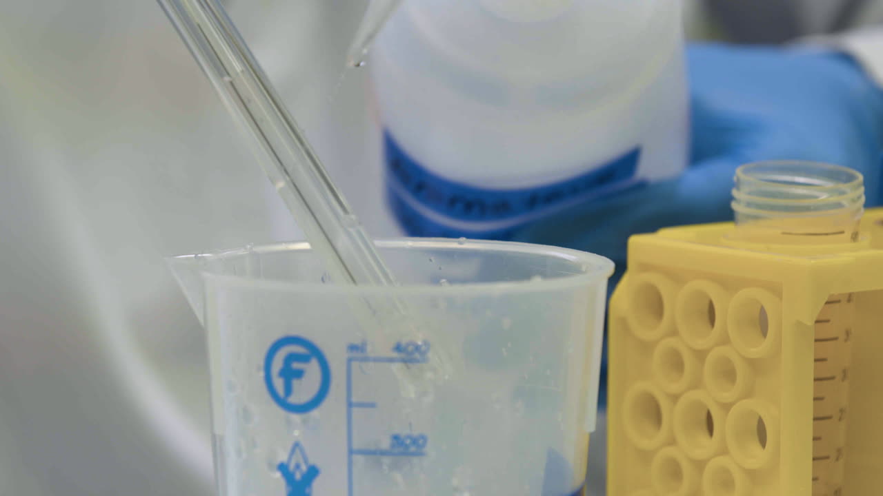 Close shot of a laboratory technician using a wash bottle to clean a pipette. The cleaning agent falls into a measuring beaker.
