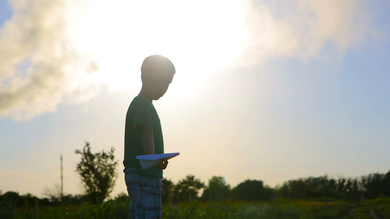 Boy With Paper Planes. Paper blue airplane in children hands at sunset near smoky pipes