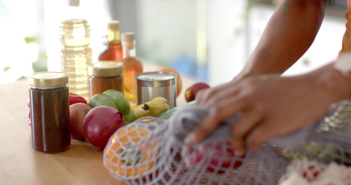 Woman lifting jam jar and activating floating code while packing produce into reusable kitchen bag