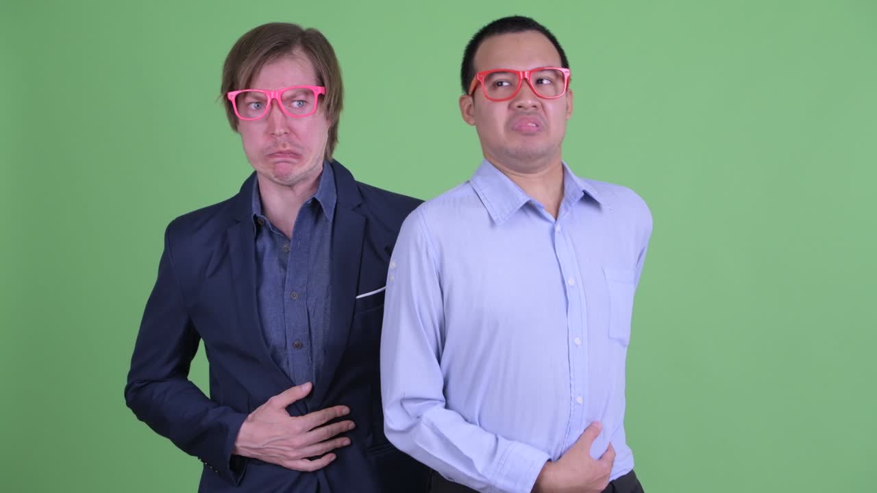 Two businessman having stomachache against green studio background