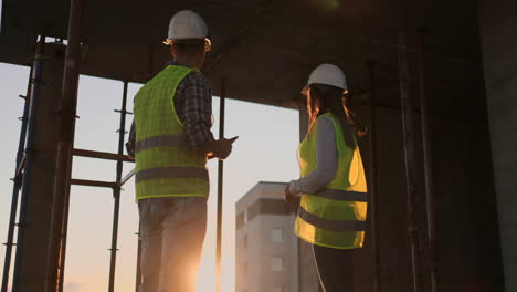 hombre y mujer trabajadores de la construcción guapos en cascos y chalecos de protección están estrechando la mano mientras trabajan en el centro de la oficina