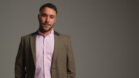 retrato de estudio de un maestro de sexo masculino maduro sonriente con chaqueta de pie contra un fondo gris disparado en cámara lenta