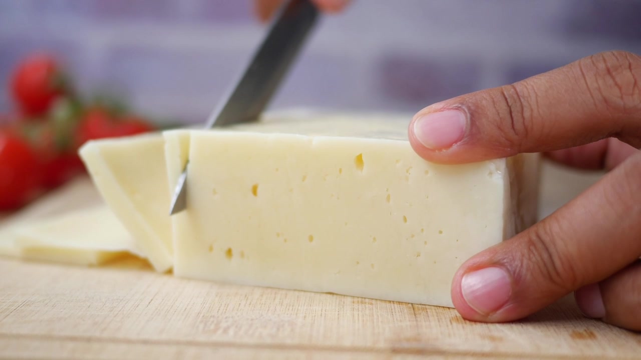 Persona che affetta un pezzo di formaggio su un tagliere di legno