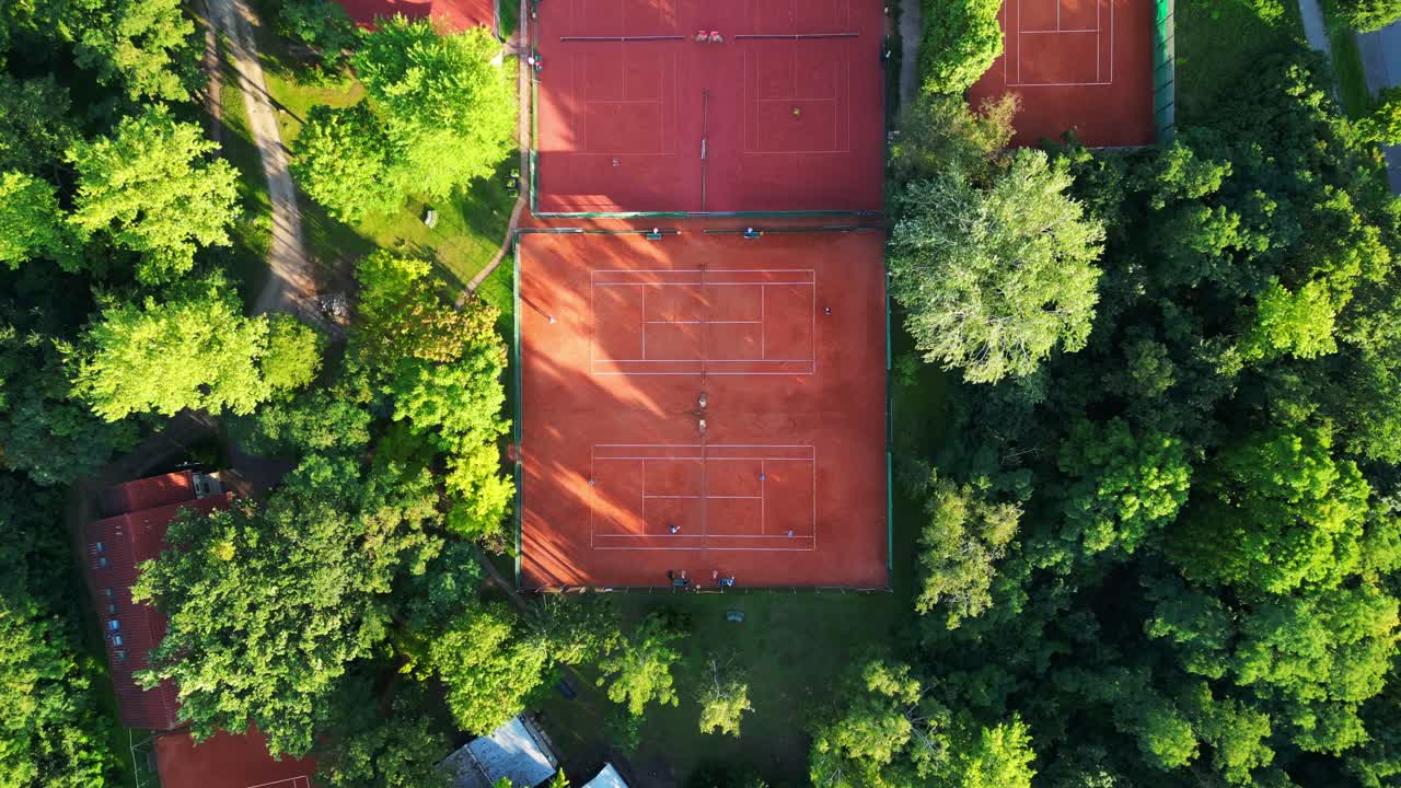 Persone che giocano una partita di tennis su campi in terra battuta durante una giornata di sole a Berlino, Germania. Telecamera drone in discesa puntata verso il basso.