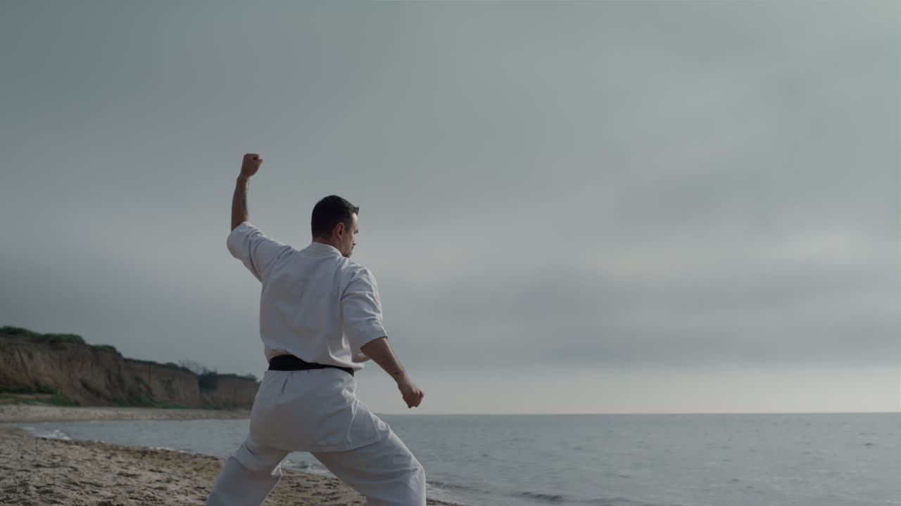 un luchador de karate entrenando fuerza en la playa. un hombre de pie en posición de combate.
