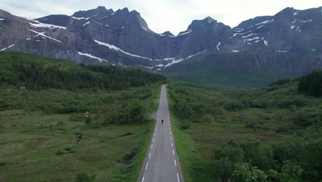 young man skating on an empty road with a scenic mountain view in background during midnight sun season