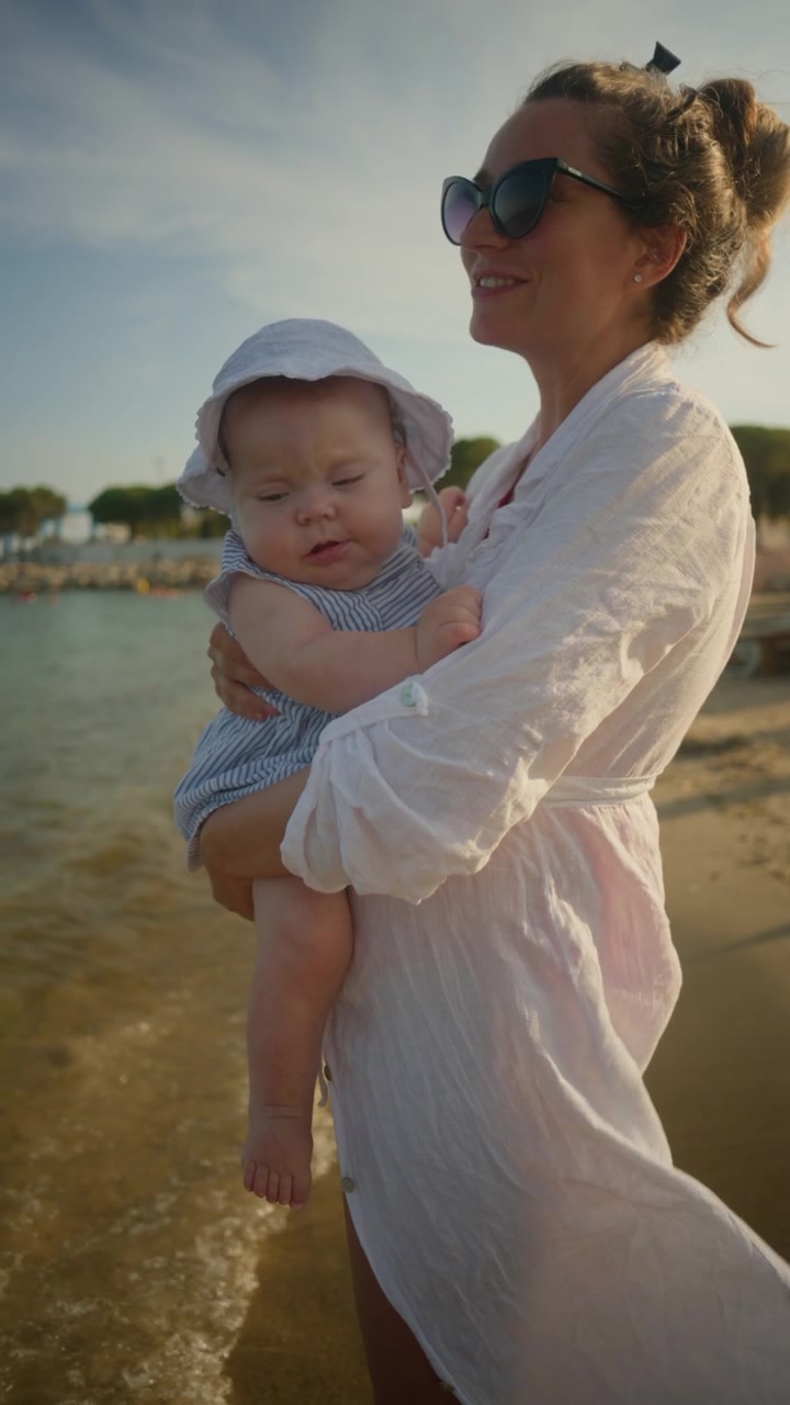 Mutter wiegt ihr schlafendes Baby an einem sonnigen Strand, genießt einen Sommerfamilienurlaub und besondere Bindungsmomente.