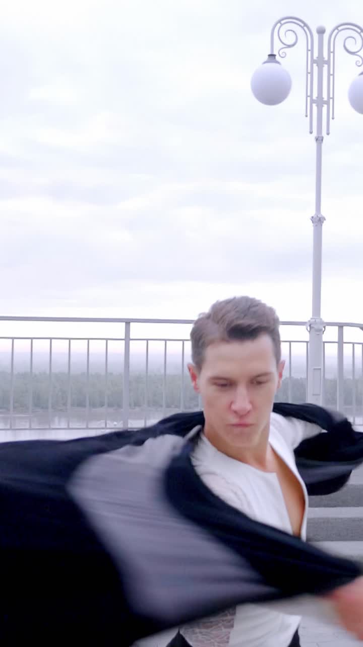 Male dancer in white shirt performing dynamic movement on outdoor staircase with urban backdrop