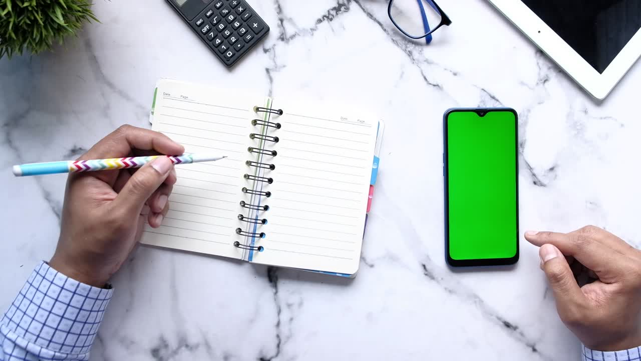 top view of man hand using smart phone and writing on notepad