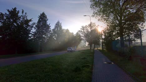 Ein-Weißes-Auto,-Das-An-Einem-Sonnigen-Morgen-Auf-Einer-Straße-Fährt,-Die-Von-Den-Sonnenstrahlen-Beleuchtet-Wird,-Die-Durch-Die-Bäume-Scheinen