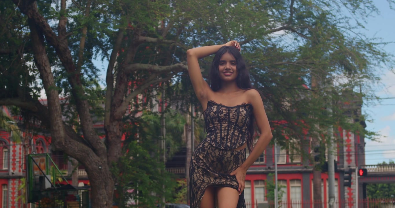 Elegante donna sudasiatica che cammina lungo un sentiero di palme baciato dal sole in abito nero