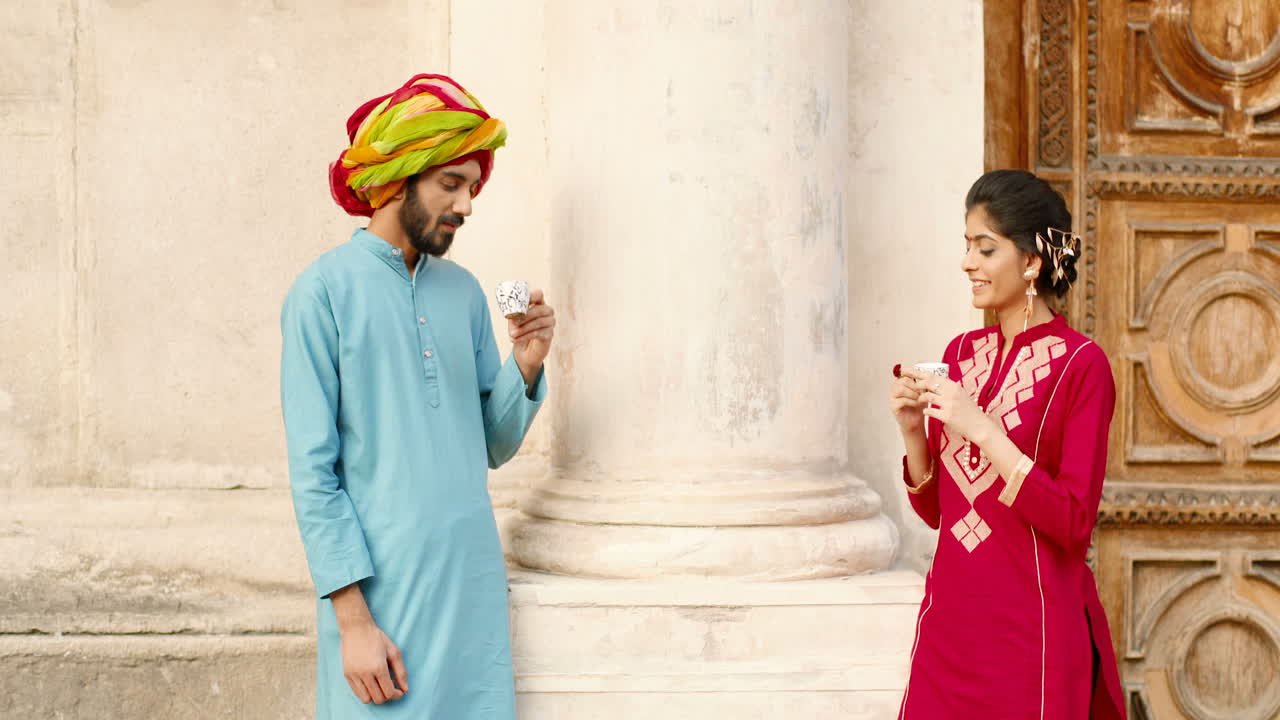 индуистская счастливая женщина с точкой на лбу и мужчина в тюрбане стоят на открытом воздухе, разговаривают и пьют кофе или чай. отдыхают. красивый мужчина и красивая женщина пьют и проводят время вместе.