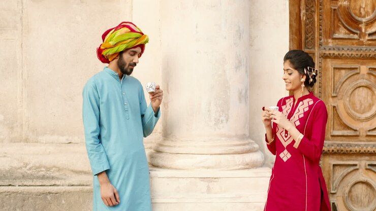 Hindu happy woman with dot on forehead and man in turban standing outdoors, talking and drinking coffe or tea. Resting. Handsome male and beautiful female sipping drink and spending time together.