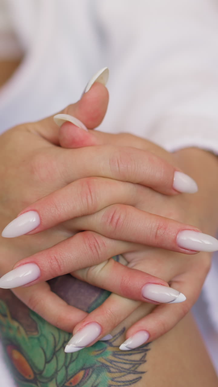Young woman with elegant manicure and stylish tattoos on leg wearing white bathrobe sits in light room extreme close view slow motion