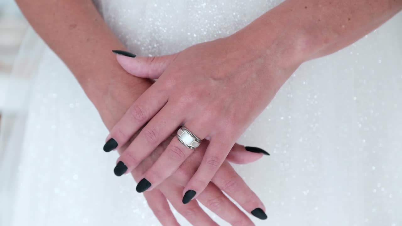 Woman in a white dress with black nails and a silver ring