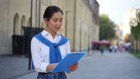 Mujer-Que-Trabaja-En-La-Calle-Leyendo-Documentos-En-Un-Portapapeles