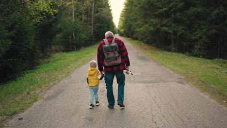 vecchio con zaino sta tenendo la mano del suo piccolo nipote che cammina insieme sulla strada attraverso la vista posteriore della foresta