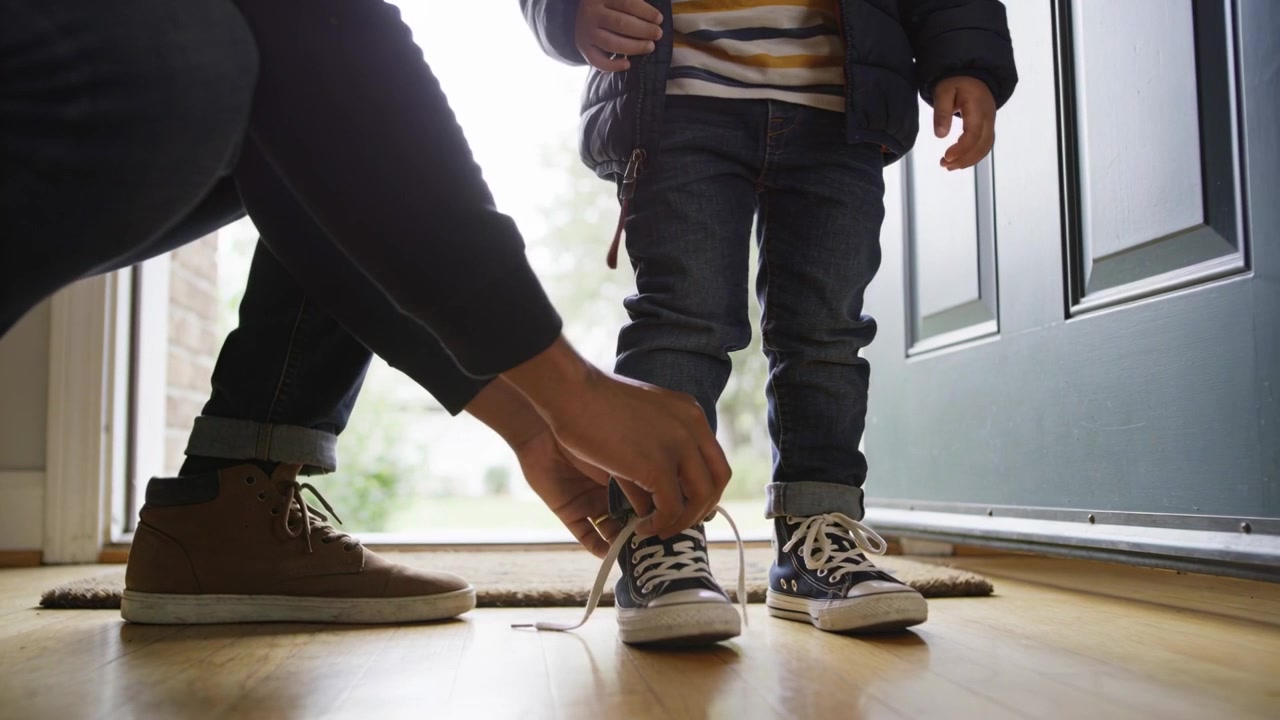 Tying kneeling parent securing child's navy high-top sneakers at open front door
