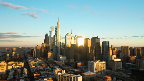 rotating aerial drone view of the downtown philadelphia skyline featuring tall, glass skyscrapers at sunset with golden light and blue summer skies showing the comcast technology center