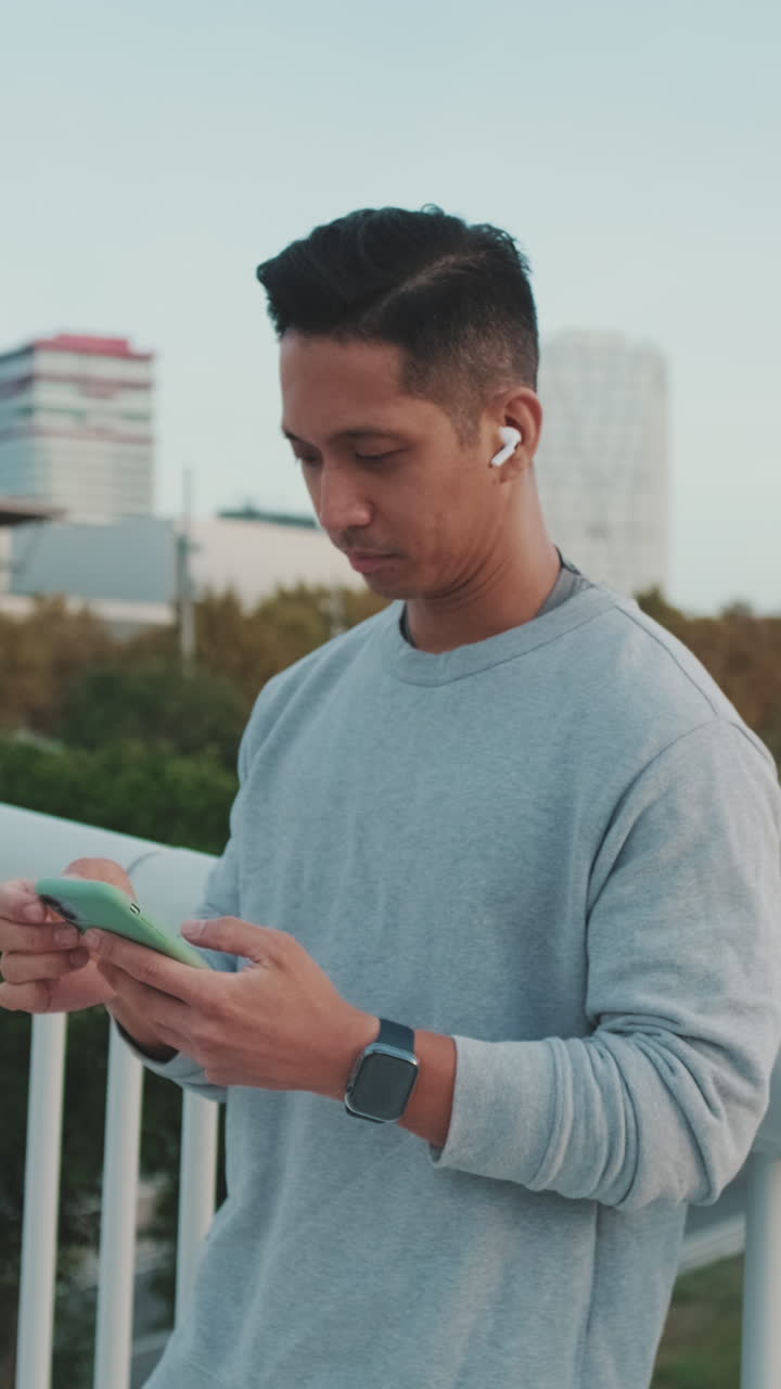 Man using phone with earbuds and smartwatch in urban setting