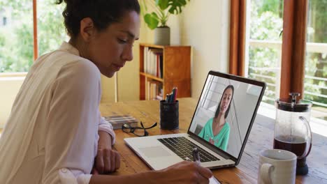 Mixed-race-businesswoman-sitting-at-desk-using-laptop-having-video-call-with-female-colleague