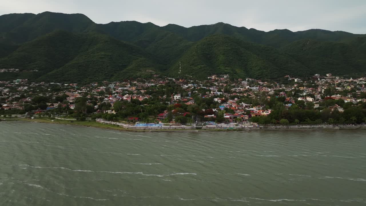 Ajijic village along Lake Chapala with lush green mountains in the background, Jalisco, Mexico. Pan left, backward dolly panoramic drone aerial