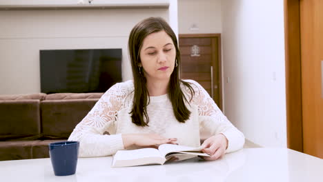 mujer caucásica lee un libro en la mesa del comedor
