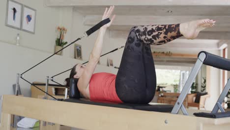 fit senior caucasian woman stretching on reformer in pilates studio, unaltered, in slow motion