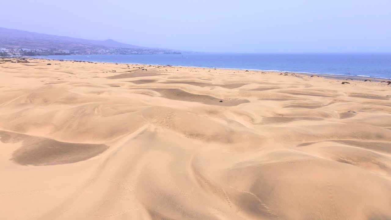Sand dunes desert against seascape in Maspalomas Gran Canaria deserts near seashore. Aerial drone view of tourists walking thorugh the dunes of Maspalomas in Gran Canaria during a windy day.