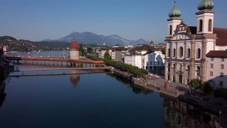 Slow-flight-over-the-river-Reuss-of-Lucern-showing-Jesuitenkirchethe-in-historic-center-and-its-bridges,-Spreuerbrücke,-Kapellbrück