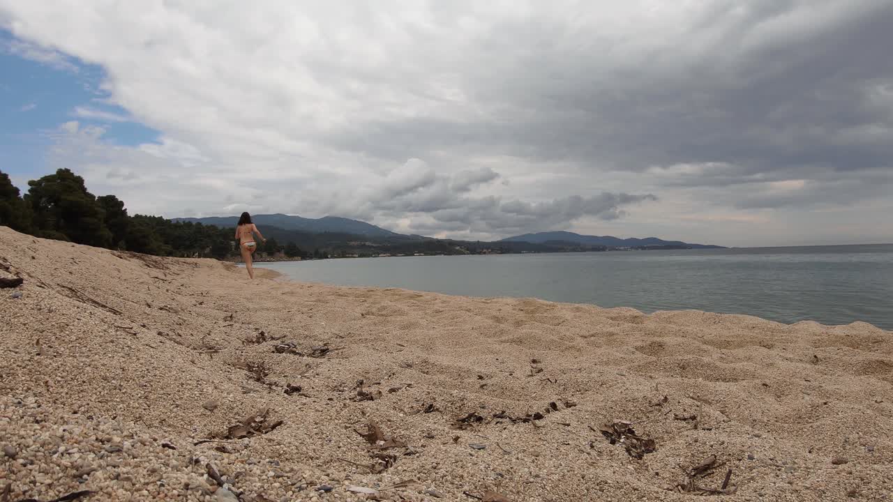 una niña corriendo en una playa en traje de baño en un día nublado