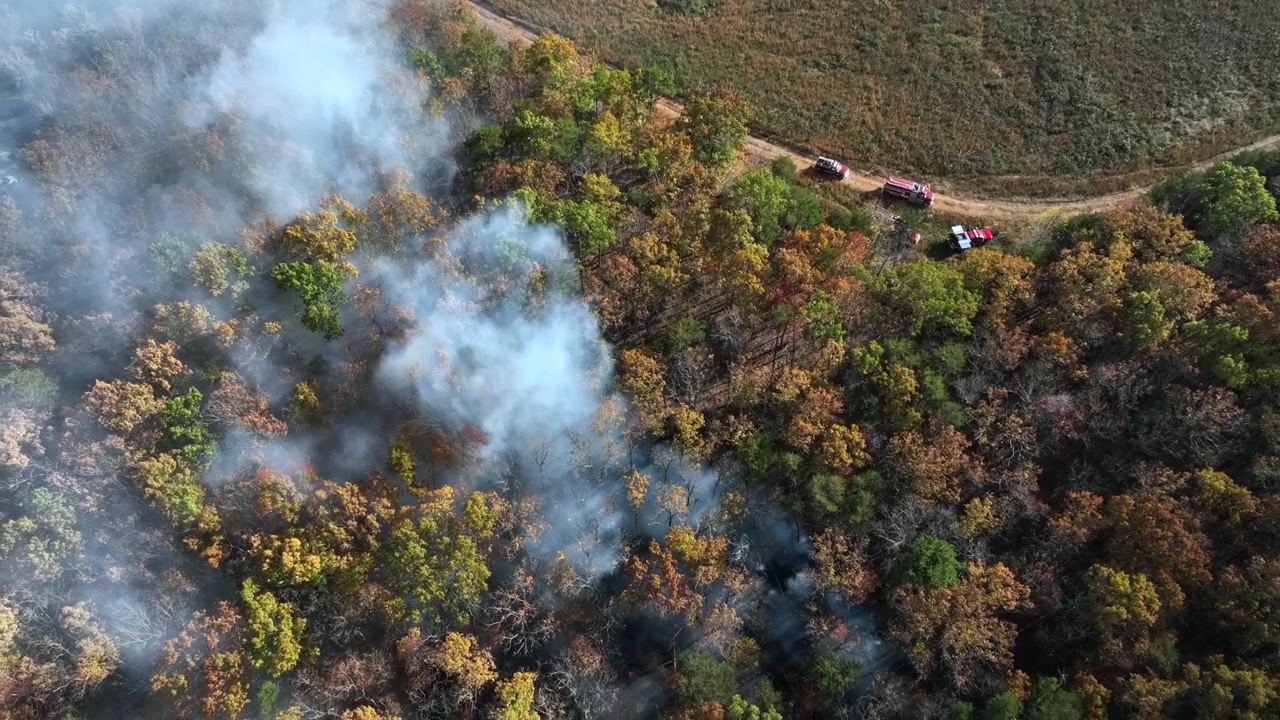 Giftig skovbrand i farverig skov i USA. Tema: Miljøforurening. Solrig efterårsdag i Vermont. Brandbil og politi på landevej. Stigende top-down droneoptagelse