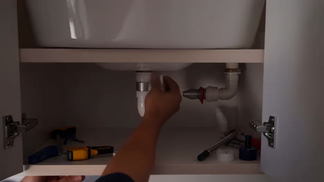 person's hand working on plumbing under a sink