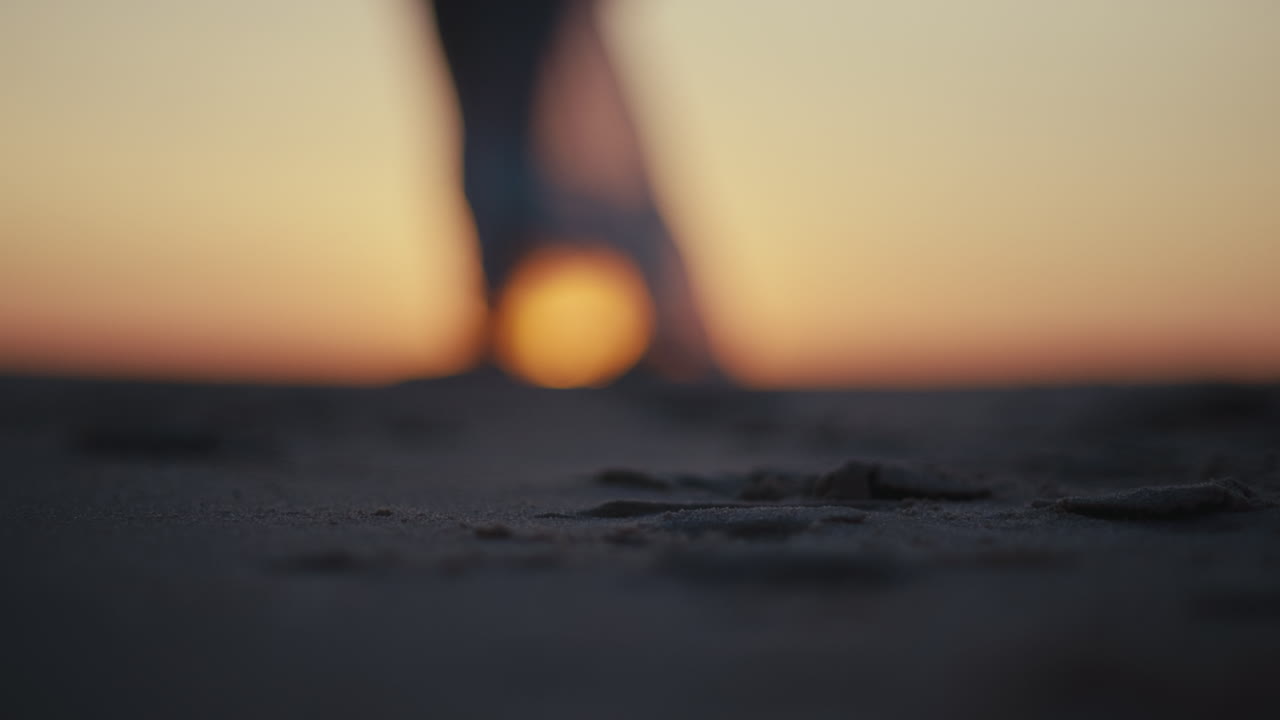 Barefoot steps on sandy beach at sunset with ocean horizon glowing in background, walking alone into dusk