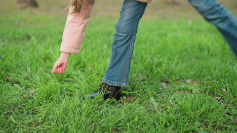 close-up of a young girl's leg in blue jeans and black shoes playing on lush green grass. she playfully uses her hand to touch the grass, capturing a moment of carefree joy and outdoor activity