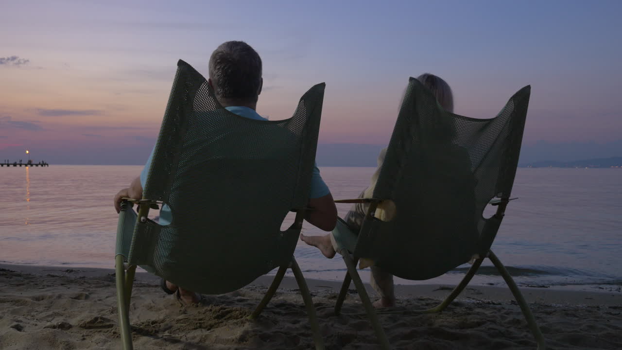 성숙한 커플이 해변에서 휴식을 취하고 테일을 마시고 있습니다.