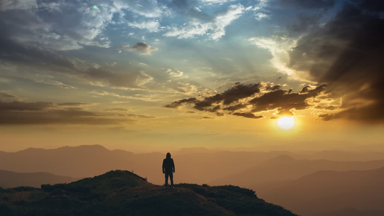 el hombre de pie en la cima de una montaña contra la brillante puesta de sol.