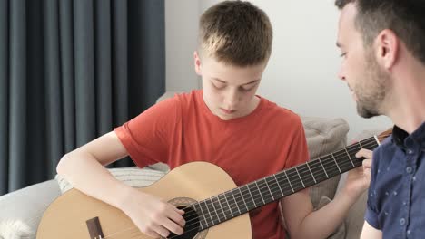 teacher instructing teenage boy playing guitar, music lesson at home.