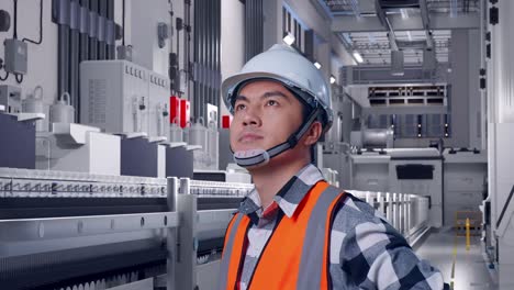 close up side view of asian male engineer wearing safety helmet looking around while standing with arms akimbo at pharmaceutical factory, vaccine production facility