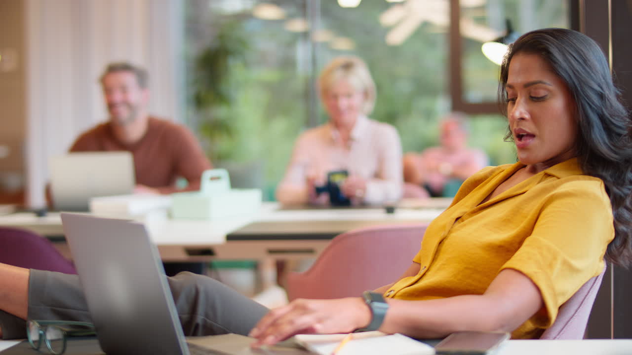 Mature Businesswoman Relaxing With Feet On Desk In Office Using Laptop