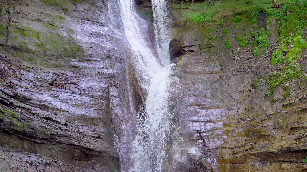 inclinación en cámara lenta hacia abajo de una cascada que cae por la pared verde de la montaña cubierta de musgo hacia una corriente de naturaleza - videografía prores 4k durante el día