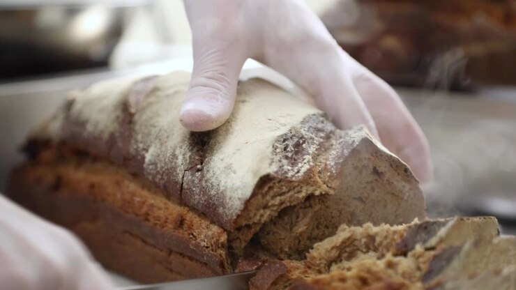 Pastry Chef's Hand In Gloves Slicing Hot And Freshly Baked Bread