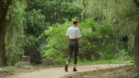 Junge-Sportliche-Frau-In-Sportkleidung,-Die-In-Einem-Park-Spaziert-Und-Morgens-Cardio-Macht---Rückansicht-In-Zeitlupe