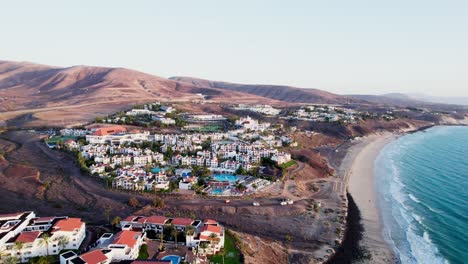 Fuerteventura-coastline-with-resorts-by-the-beach,-clear-sky,-aerial-view