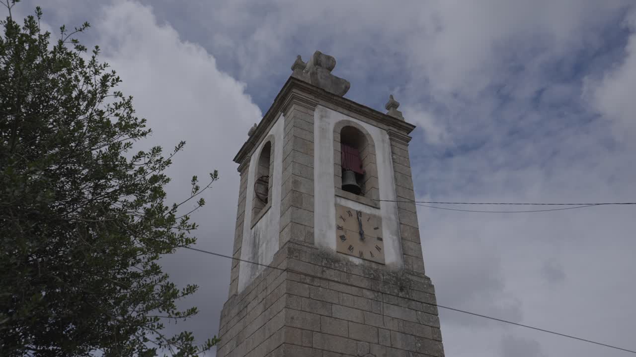 Campanile in pietra di una chiesa con orologio e archi che si erge contro un cielo nuvoloso.