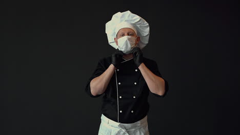 chef masculino listo para cocinar, se pone una máscara médica. disparo medio sobre fondo negro.