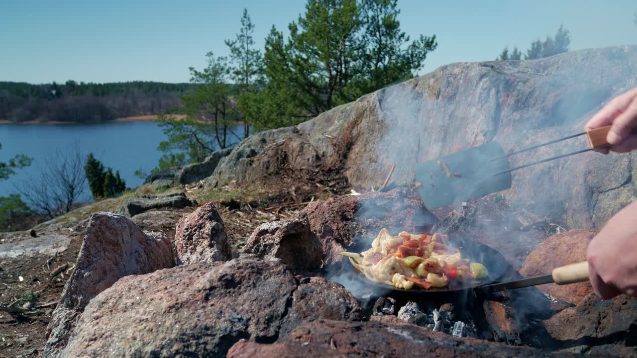 Hands cooking food on campfire frying pan a sunny day