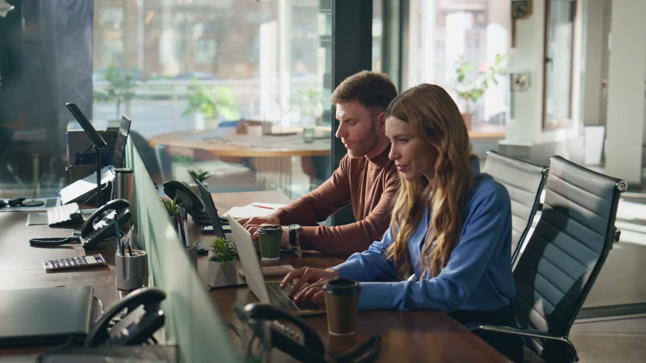 Two coworkers focused laptops creating business project together at coworking