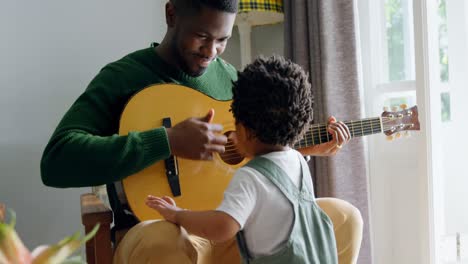 -Front-view-of-young-black-father-and-little-son-playing-guitar-in-living-room-of-comfortable-home-4