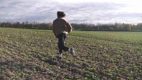 slow motion of man running across open countryside under bright sky and wind-blown field, running with joy and freedom